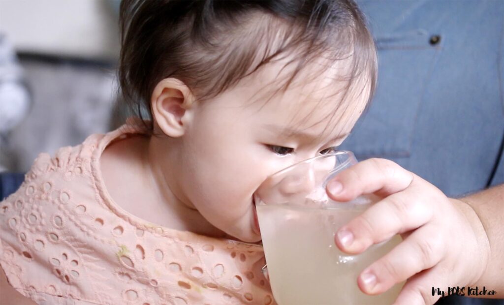 Toddler drinking sugar free lemonade from a glass.