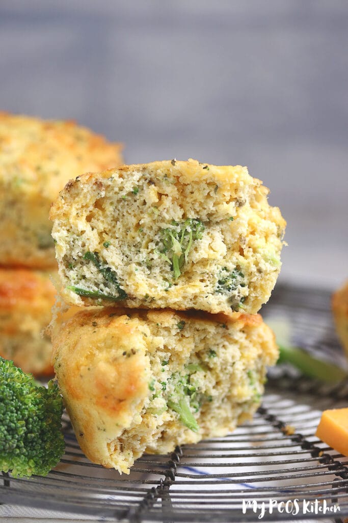 Two savory muffins on top of one another and cut in half to show the broccoli and cheese inside.