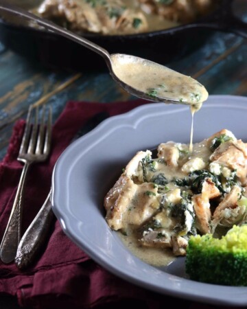 Keto Spinach & Feta Stuffed Chicken Breast with Creamy Sauce - My PCOS Kitchen - A spoonful of starch-free cream gravy is poured over stuffed chicken breasts on a plate.