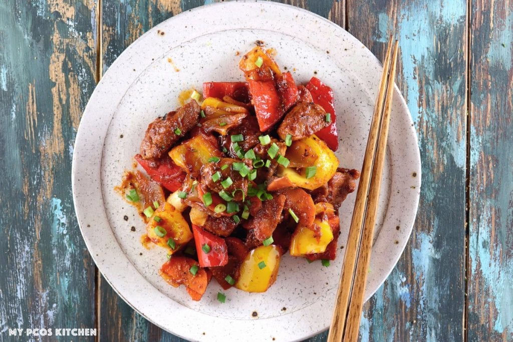 My PCOS Kitchen - Low Carb Paleo Sweet and Sour Pork - An overhead shot of a white ceramic plate and blue wood background with some gluten-free and sugar-free sweet and sour pork with peppers and onions.