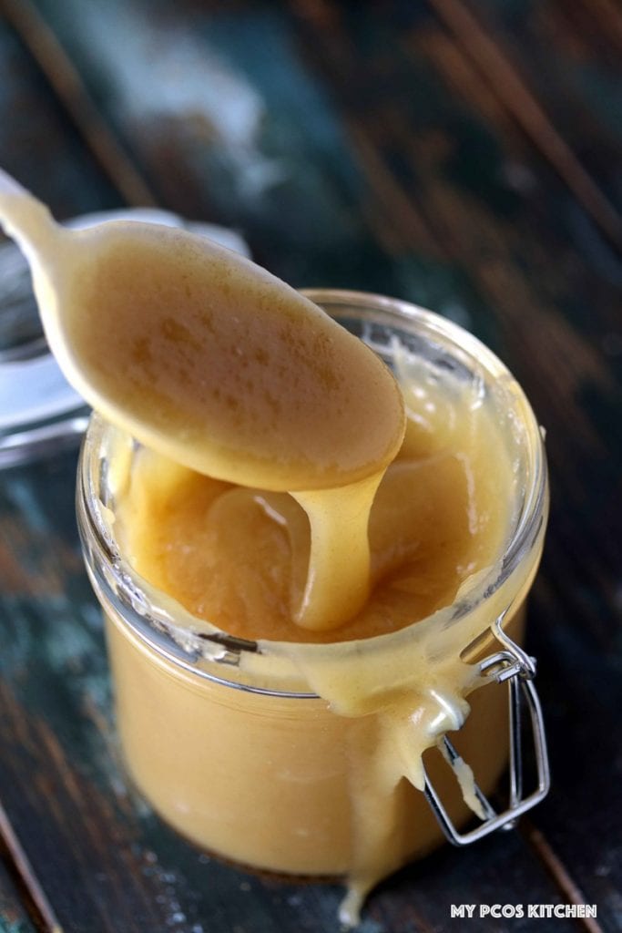 Sugar Free Caramel Sauce - My PCOS Kitchen - Caramel sauce drizzling from a white spoon into a glass jar.