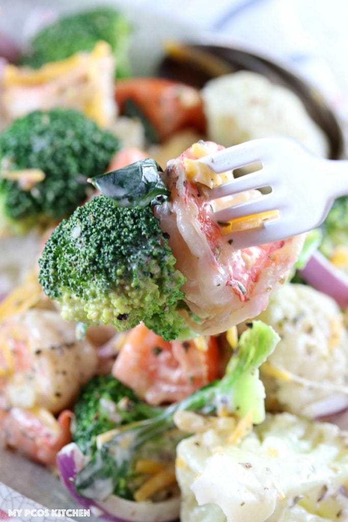 Amish Broccoli and Cauliflower Salad with Shrimps - My PCOS Kitchen - A white fork holds a piece of shrimp and broccoli with some cheddar cheese.