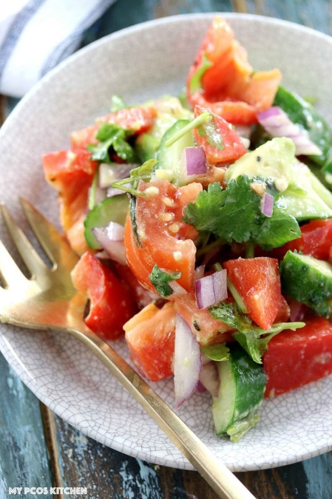 Low Carb Paleo Avocado Cucumber Tomato Salad - My PCOS Kitchen - An overhead shot of this avocado medley salad with tomatoes and fresh cilantro. Brass spoon on the side.