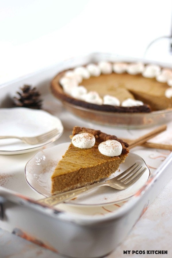 A slice of sugar free pumpkin pie on a white metal tray with a round pumpkin pie in the background.