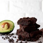 Four sugar free brownies stacked on top of one another with some avocado in the background.
