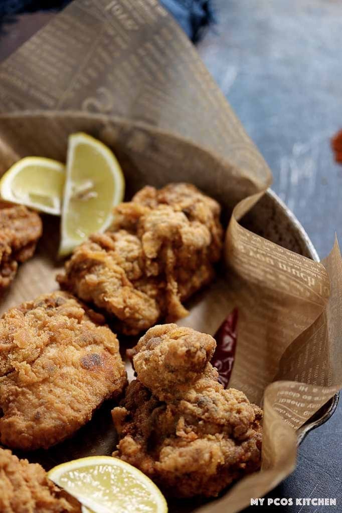 Juicy pieces of keto fried chicken with some lemon wedges in a frying pan.