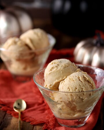 Keto pumpkin ice cream scoops inside glass bowls served on a wooden table.
