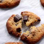 A chewy keto chocolate chip cookie gently split in 3 with melted sugar free chocolate bars on top.