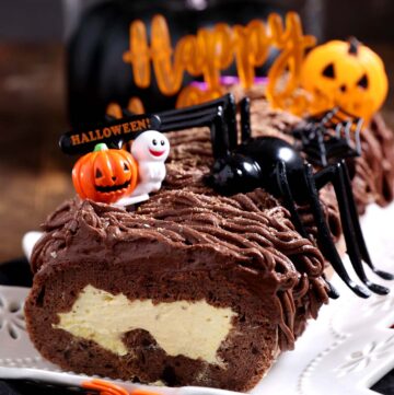 A keto gluten free swiss roll filled with pumpkin cream and chocolate frosting decorated with halloween props.