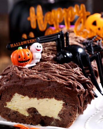 A keto gluten free swiss roll filled with pumpkin cream and chocolate frosting decorated with halloween props.